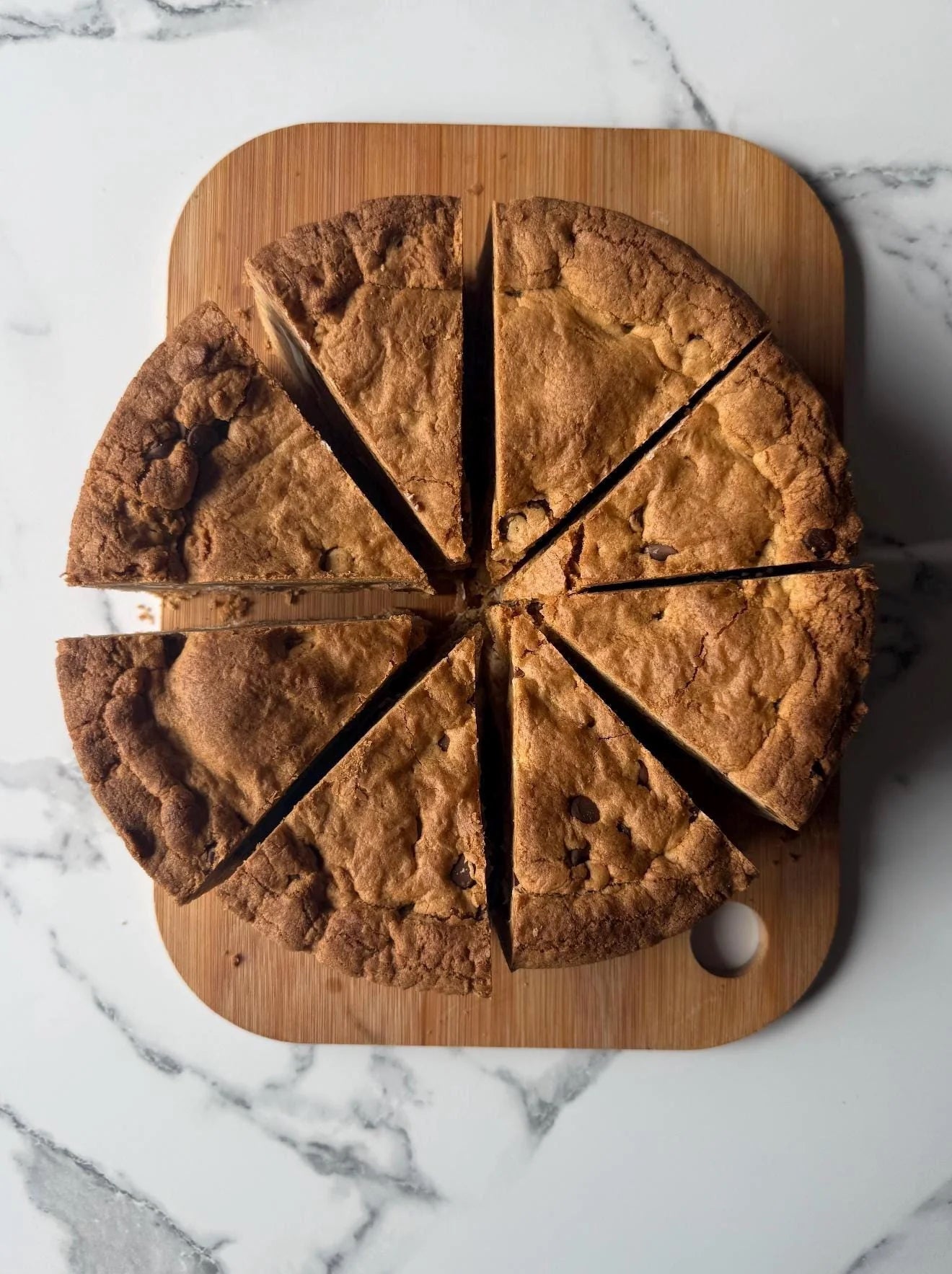 Cookie pie sliced into pieces on a wooden board with a marble background